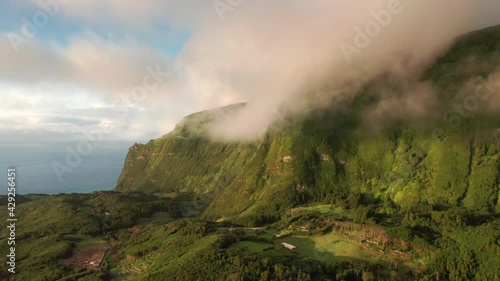 Drone shot of mountains landscape of Poco Ribeira do Ferreiro, Alagoinha, Flores Island, Azores, Portugal, Europe. Overhead view of green cliffs covered white clouds, 4k footage