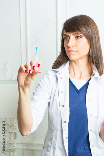 brunette medical attendant wearing white and blue doctor's overall is standing with antlia in her hand photo