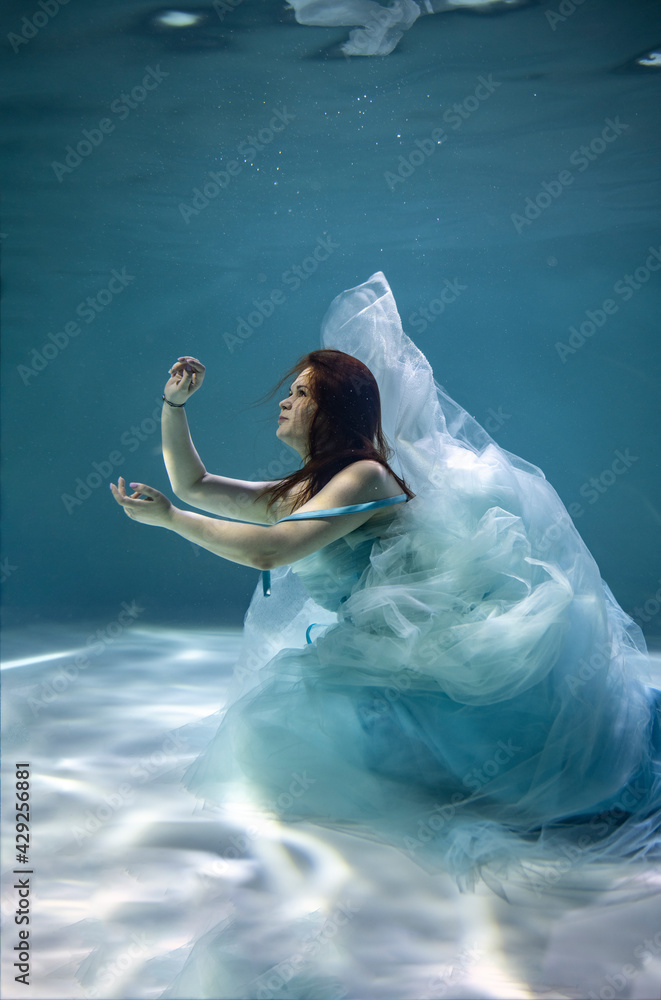 beautiful girl with red hair in a ball gown blue dress underwater on a blue background beautiful girl with red hair in a ball gown blue dress underwater on a blue background