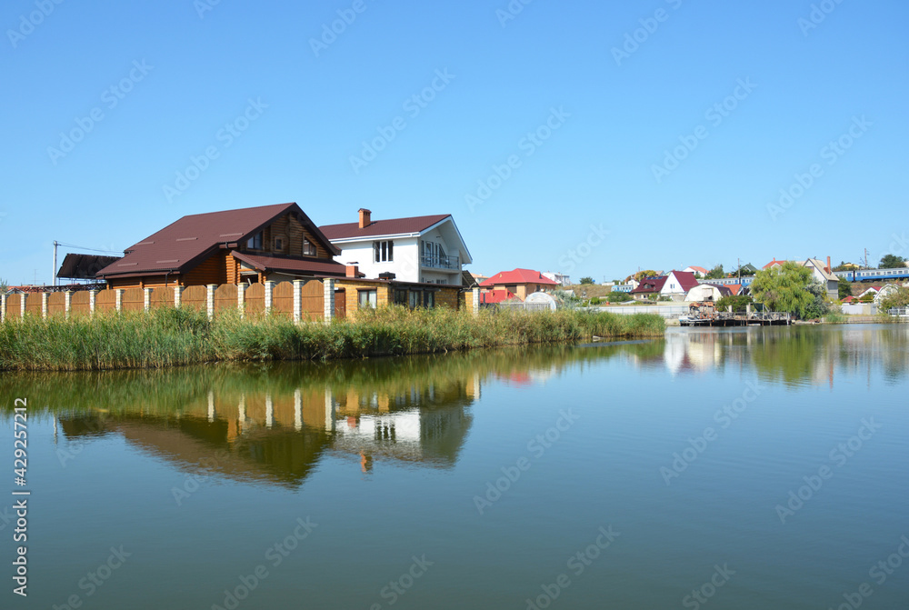 Modern cottage houses reflected in the water built on the bank of the lake or river. Constructing houses along the river with a beautiful view on the river.