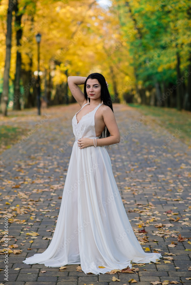 Beautiful brunette young female in white dress in autumn park