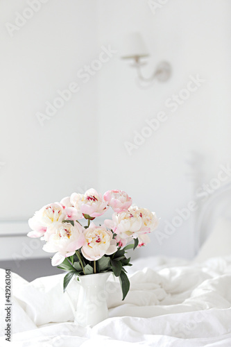Bouquet of pink peonies on white bed linen. Modern interior in the bedroom. Wedding and festive style. © Kotkoa