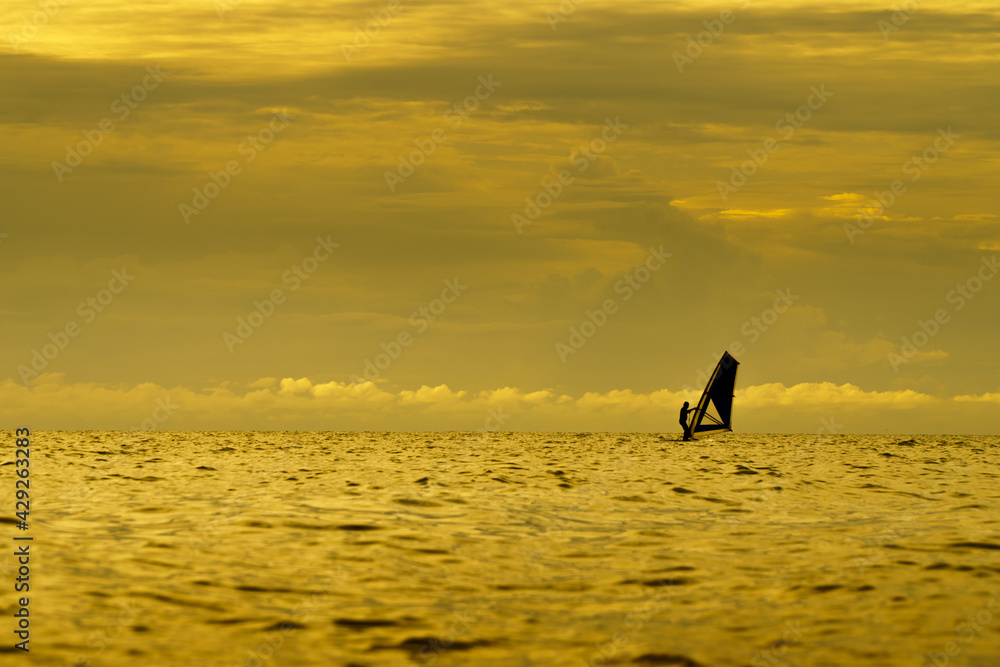 The golden silhouette of a windsurfer playing surfing board in the sea at sunset.