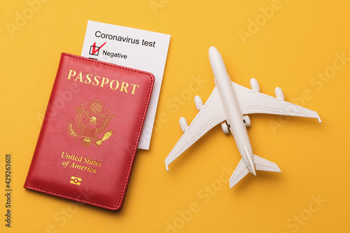 Toy plane, American passport and coronavirus test results on a yellow background, top view