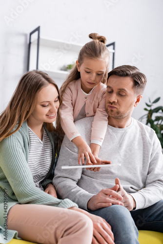 Kid using digital tablet near parents on couch.