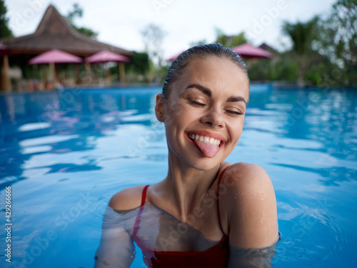 happy woman swims in clear pool water and shows tongue to model cropped view