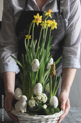 Easter floral composition for table centerpiece with yellow narcissus, festive eggs, moss and bunny. Floral spring workshop. photo