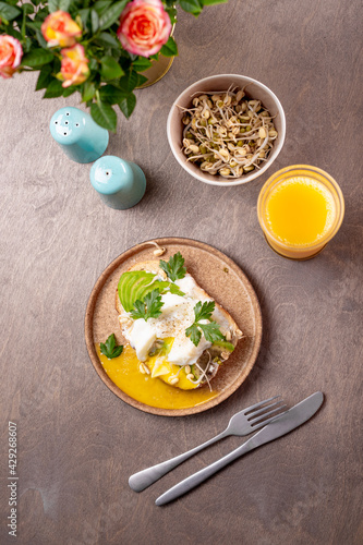 Light summer breakfast - sandwich with avocado, cottage cheese, sprouted beans and poached egg with orange juice on the table