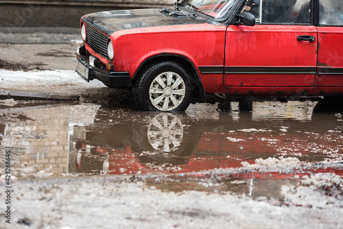 Old red car and huge puddle on winter city street road