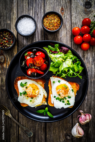 Continental breakfast - sunny side up eggs on toasted bread with fresh vegetable salad on wooden table