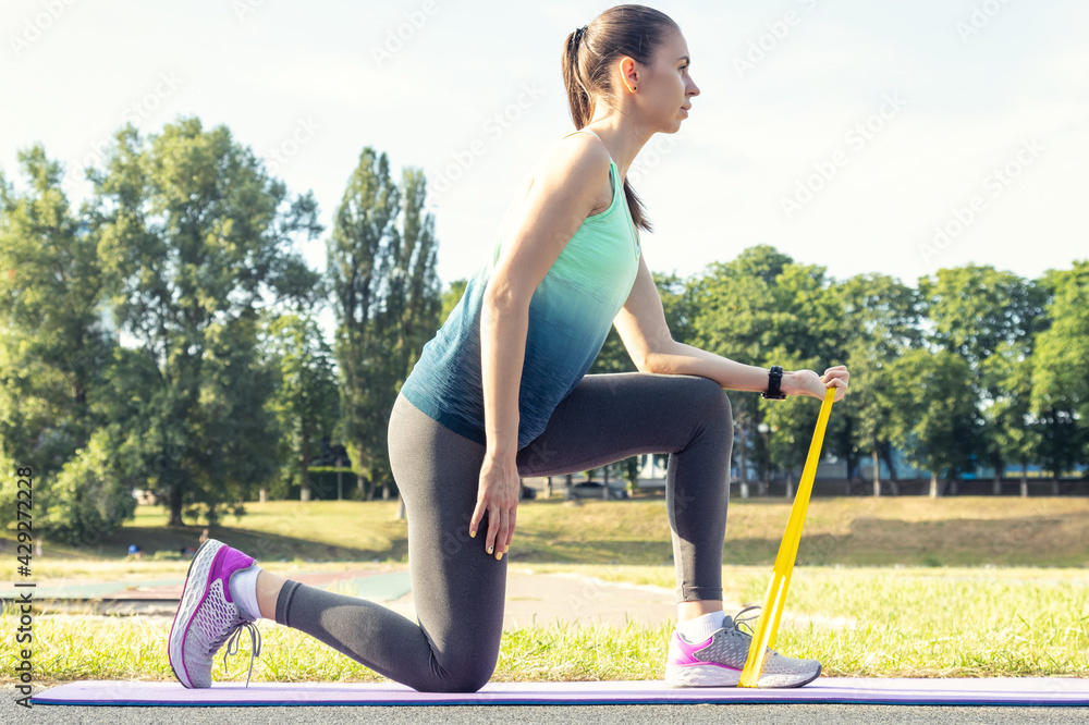 Fototapeta premium Young woman is engaged with fit elastic band on a fitness mat. Exercise to strengthen the muscles of the arms.