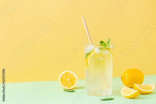 Lemon ice tea with mint leaves on bicolor background (yellow and green). Fresh exotic cocktail in tall glass. Copy space.