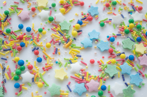 Multi-color festive background of a scattering of sugar candy sprinkles for cupcakes and other pastries in form of stars, sticks and balls. Pastel colors of red, pink and green, blue and yellow