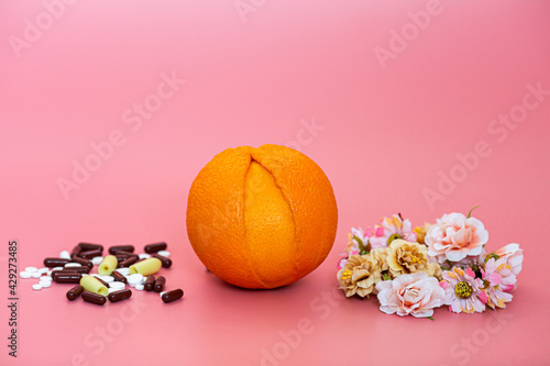 Ugly orange on a pink background with medicines and flowers. The concept of treatment and prevention of vaginal diseases. photo