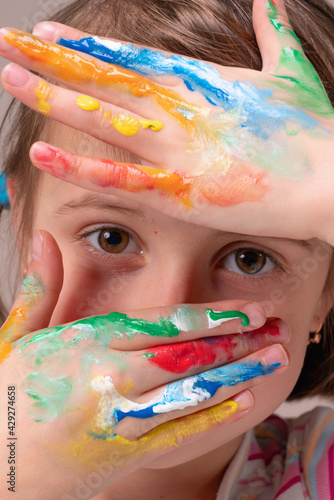 Colour, children and cognition concept. Close up portrait of beautiful young girl with colorful painted hands.