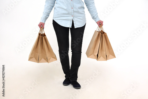 A girl in denim clothes with three paper bags in each hand on a white background