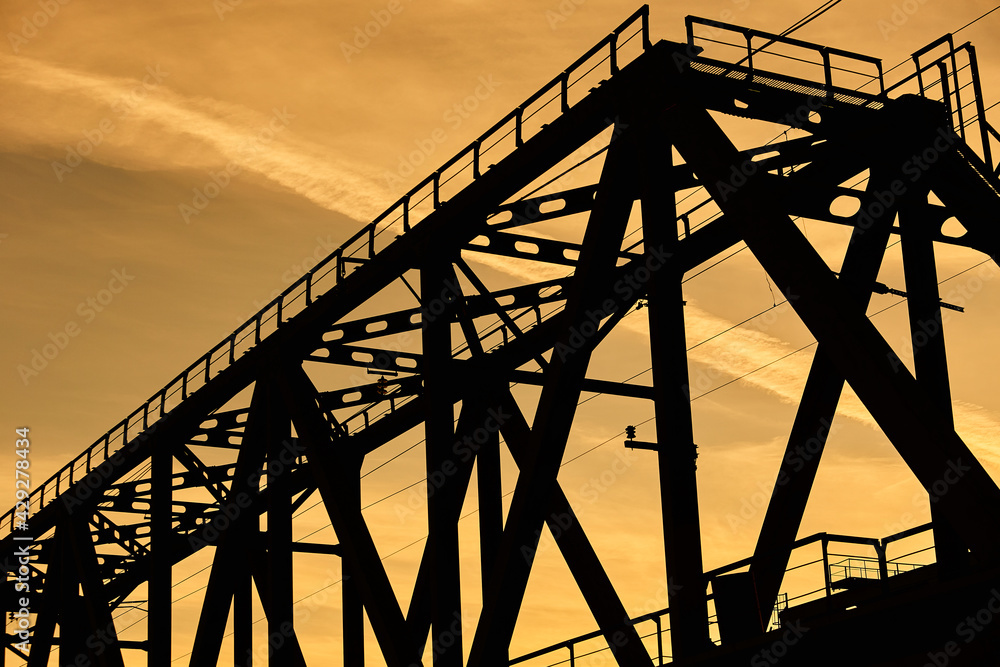 The silhouette of the metal structure of the railway bridge at sunset. Engineering structure made of steel against the sky. The silhouette of the metal structure of the railway bridge at sunset. Engineering structure made of steel against the sky.