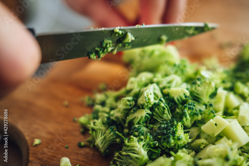 Closeup of a female chopping the fresh and tasty broccoli with a knife on a wooden cutting board