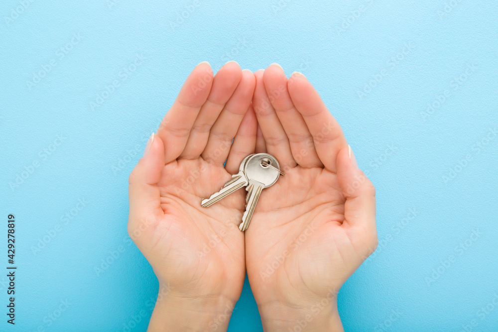 Two metal door keys on young adult woman palms on light blue table background. Pastel color. Closeup. Point of view shot. Top down view.