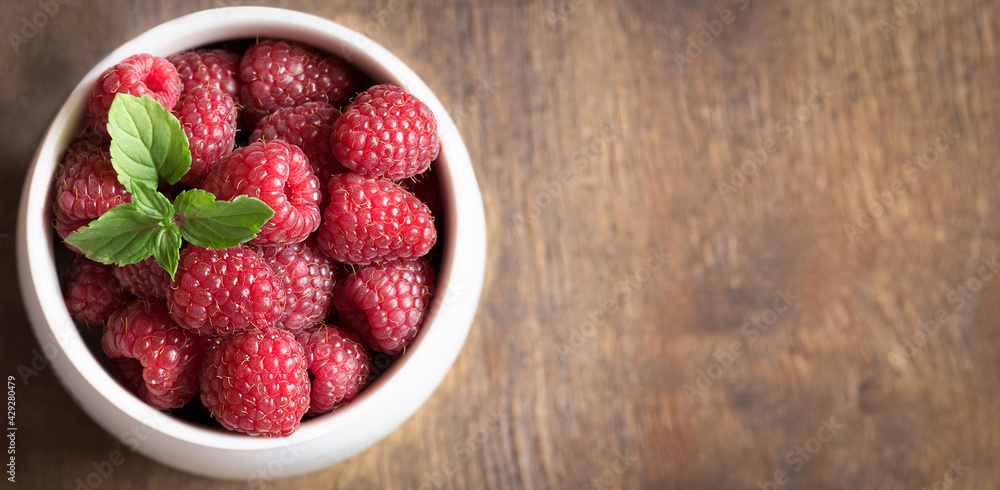 Ripe fresh raspberries in a white bowl on a brown wooden background. Ripe fresh raspberries in a white bowl on a brown wooden background.