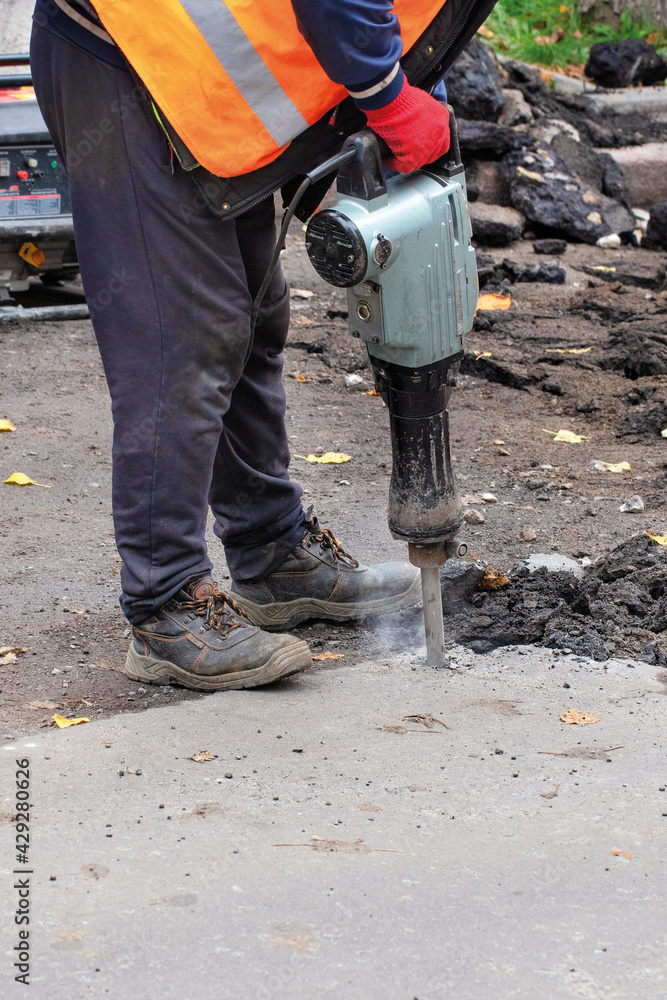 A worker breaks up old asphalt with an electric jackhammer. A worker breaks up old asphalt with an electric jackhammer.