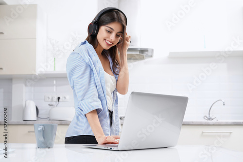 Smiling young woman smiling and working in laptop in kitchen. Concept of working at home.