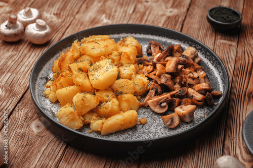 Vegetarian dish fried potatoes with mushrooms served unmixed in a concrete plate