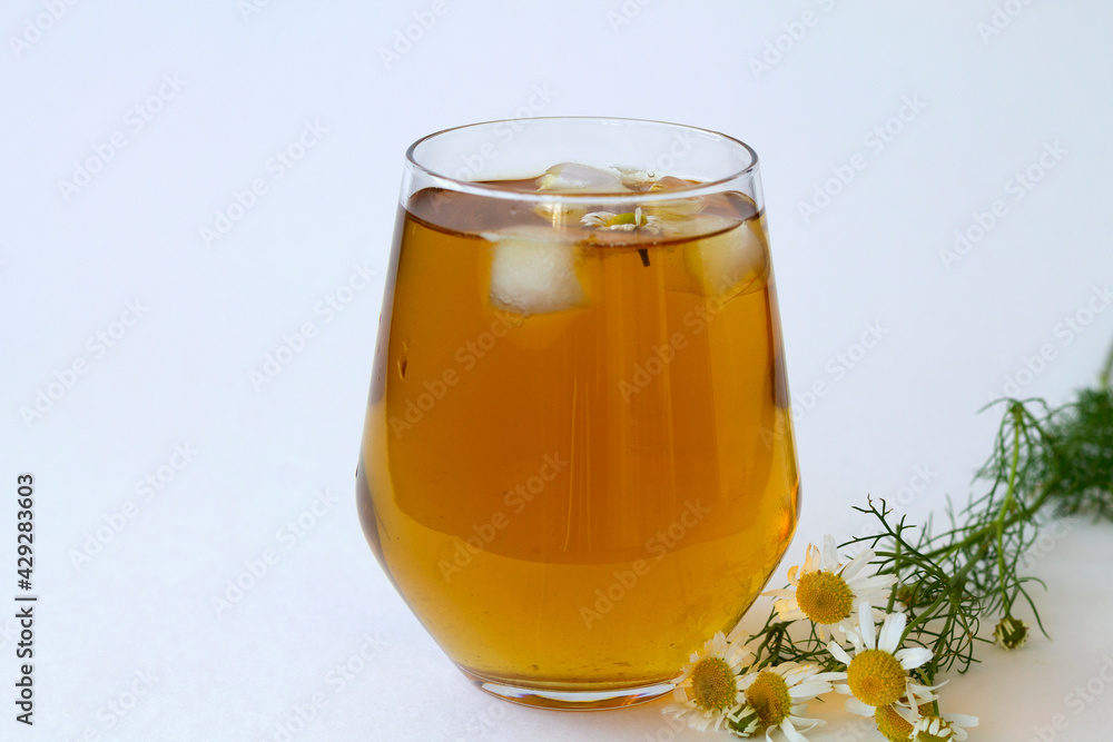 chamomile tea. glass cup of iced Herbal chamomile tea on a white table with copy space. cup of tea with fresh flowers and green leaves on white background. chamomile tea. glass cup of iced Herbal chamomile tea on a white table with copy space. cup of tea with fresh flowers and green leaves on white background.