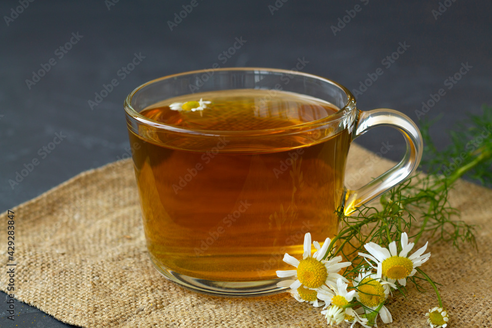 hot drinks. mug of chamomile tea on sackloth. glass cup of iced Herbal chamomile tea on a black table with copy space. cup of tea with fresh flowers and green leaves on grey background. hot drinks. mug of chamomile tea on sackloth. glass cup of iced Herbal chamomile tea on a black table with copy space. cup of tea with fresh flowers and green leaves on grey background.