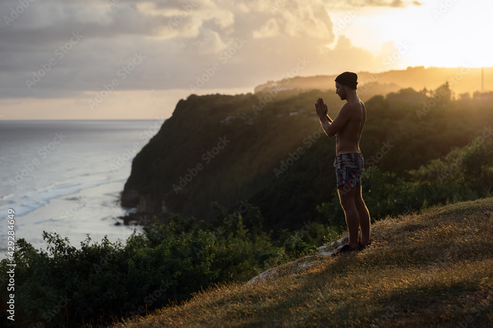 A man meditates on a cliff face with a stunning view.