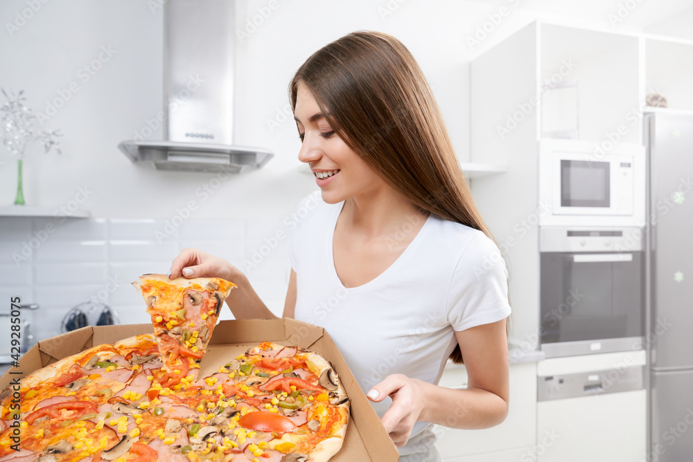 Side view of beautiful woman holding big tasty pizza in kitchen. Concept of lunch at home.