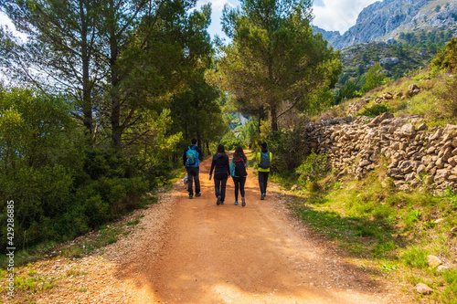 People walking along a path, near the Sierra de Bernia mountains, on a spring day, with cloudy skies.