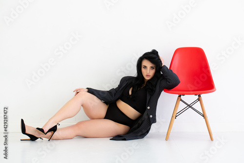 Brunette lying on white background. Red chair. Office suitecase. Fashion european girl.