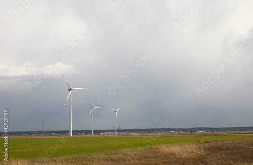 Wind turbines, three modern windmills on a green field before the storm