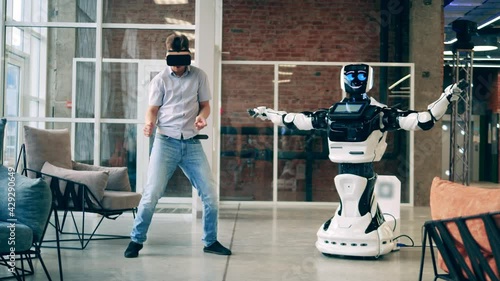 Human and robot communication concept. Businessman is wearing VR-glasses while dancing next to a cyborg photo