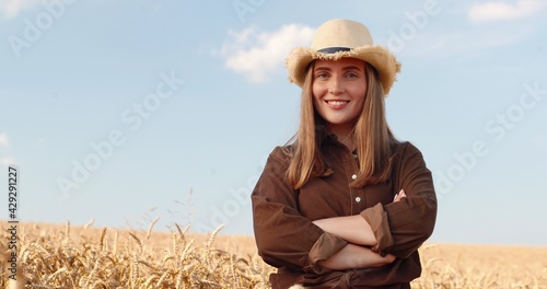 Fotografie Portrait of pretty cheerful young female standing in golden wheat field and smiling to camera in good mood