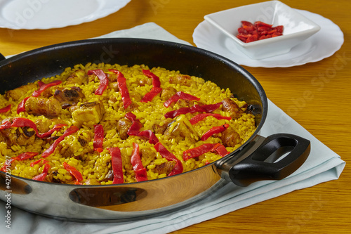 Traditional spanish and tasty seafood paella with pork sausages, pork ribs and red peppers in frying pan decorated with a  plate of red pepper and a spoon.