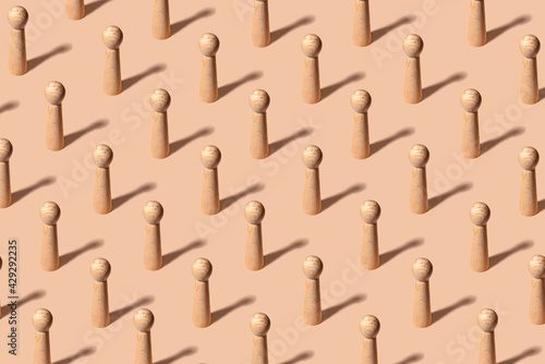 Creative pattern with equal wooden figures representing people on pastel orange background - concept of uniformity photo