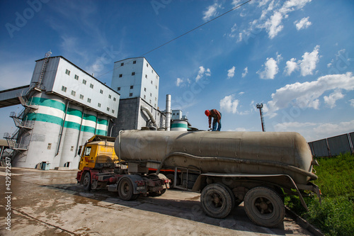 Standard Cement plant. Concrete silos and industrial buildings. Cement truck with worker on foreground. Panorama view.