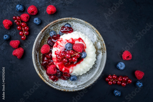 Modern style traditional blancmange almond pudding with wild berry coulis served as top view in a Nordic design plate on black background photo