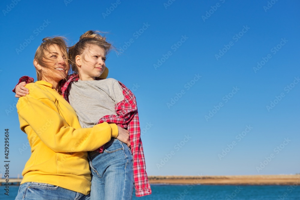 Outdoor portrait of happy mom and child daughter hugging together, blue sky background