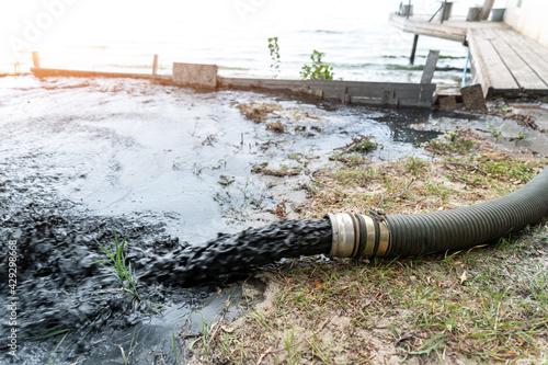 Close-up big pipe of power pump machine pouring mud sludge waste water with sand and silt on ground. Sand-wash and coast-depeening. Septic sewage maintenance service. Industrial environment pollution