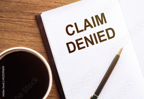 CLAIM DENIED - text on notepad on wooden desk.