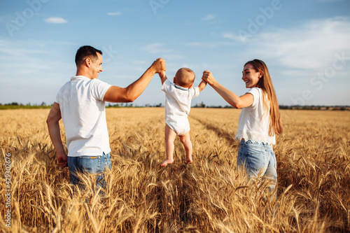 A couple with a child having fun at the middle of the golden wheat field. Father and mother hold their kid on hands making fly. Family values, happiness and togetherness concept.