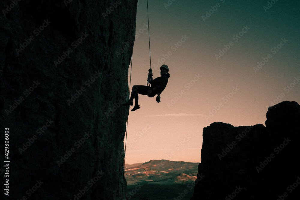 silhouette of woman rappelling held by climbing rope, at sunset in mountain landscape in Etxauri, Navarra, Spain. silhouette of woman rappelling held by climbing rope, at sunset in mountain landscape in Etxauri, Navarra, Spain.