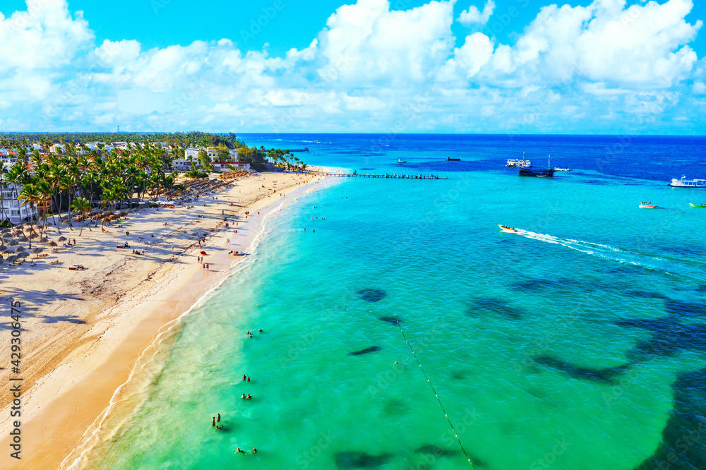 Beach vacation and travel background. Aerial drone view of beautiful atlantic tropical beach with straw umbrellas, palms and boats. Bavaro beach, Punta Cana, Dominican Republic.