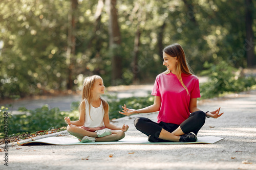 Mother with daughter doing yoga in a summer park