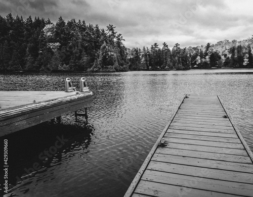 A wooden boat dock, pier, on an empty lake with trees in background. Black and white