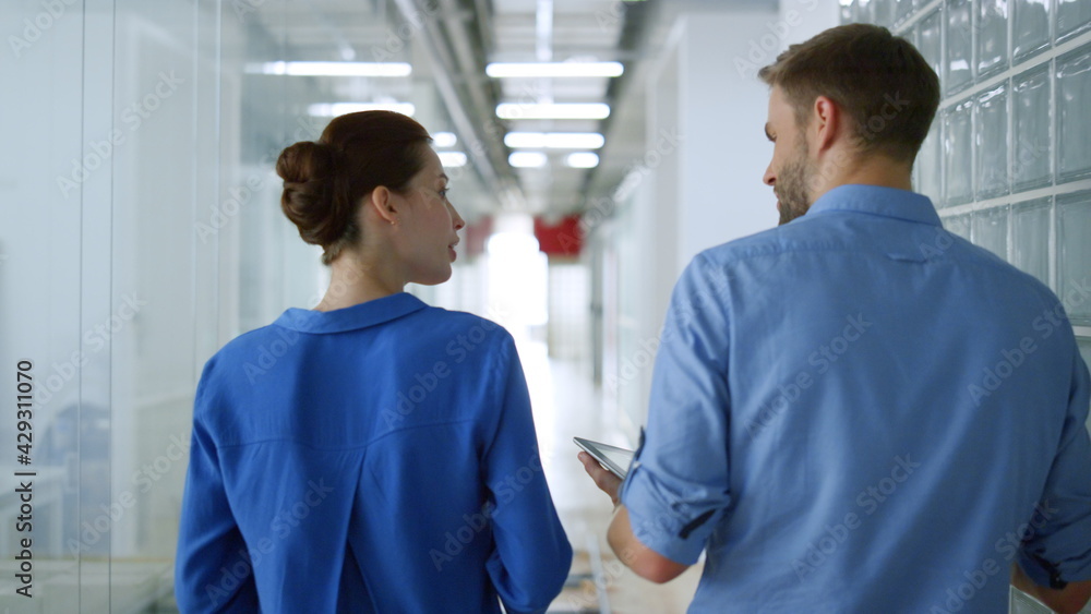 Obraz premium Back view man woman walking office. Serious business couple talking corridor