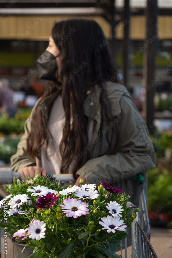 Young girl looking for plants. Flowers in a shopping cart, carried by a young girl in bokeh. Young girl looking for plants. Flowers in a shopping cart, carried by a young girl in bokeh.